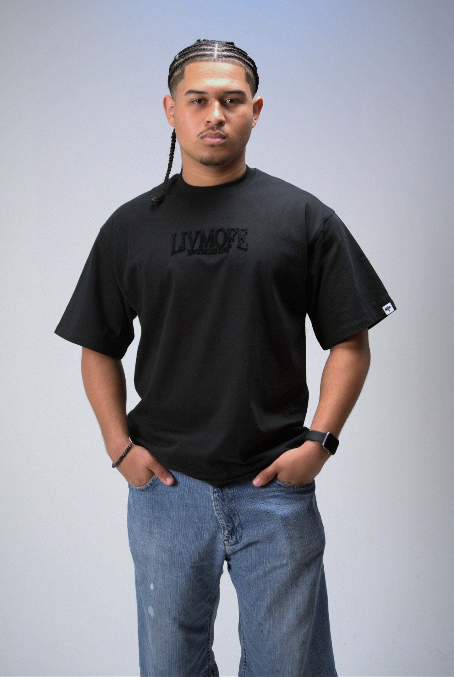 Man wearing a black t-shirt with text and blue jeans on a gray background