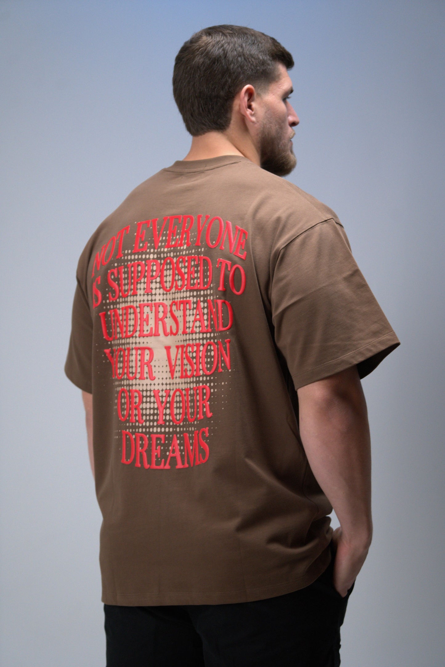 Man wearing a brown t-shirt with red text on the back 