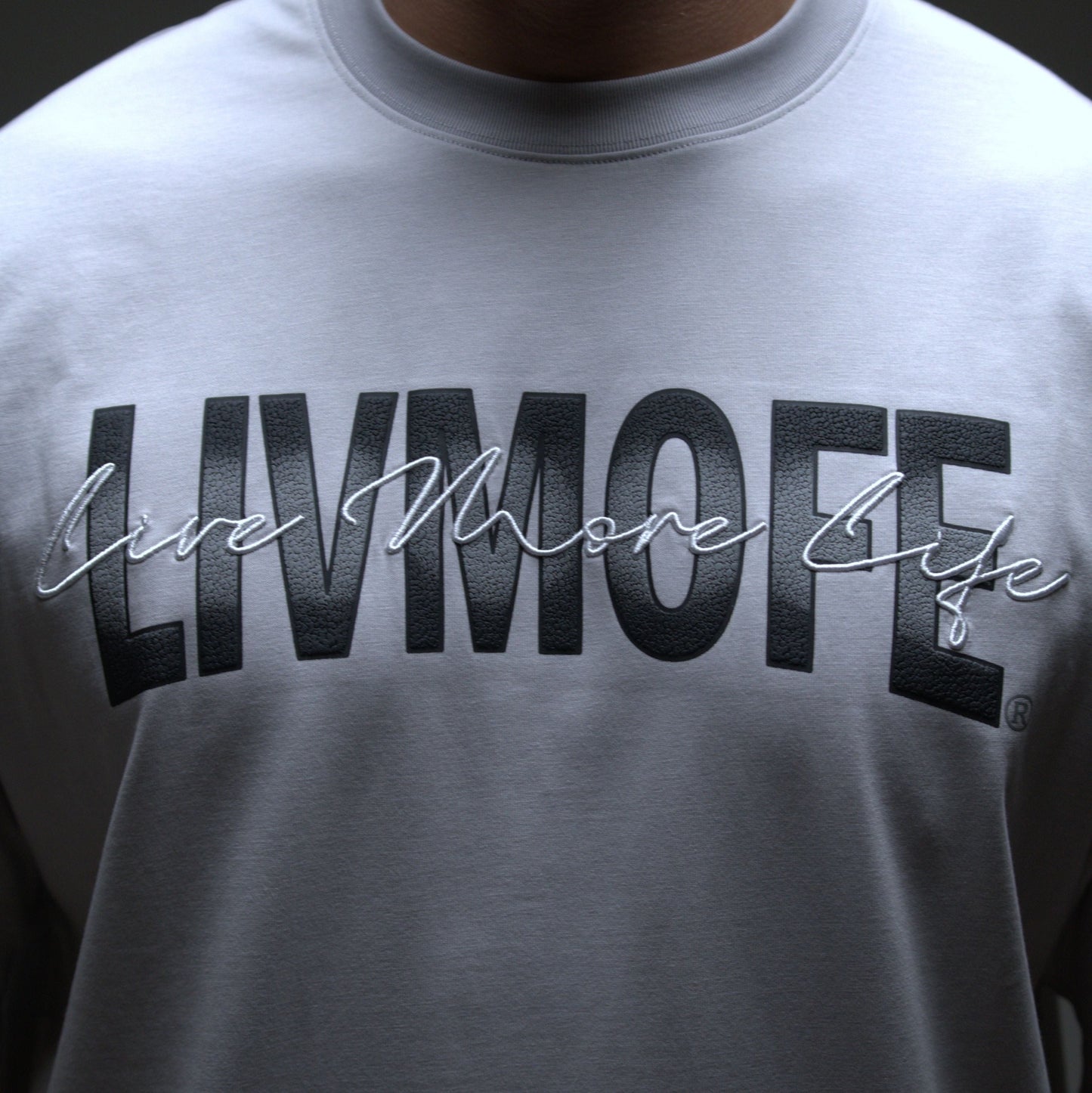 Gray sweatshirt with 'LIVMOFE' text worn by a person against a dark background
