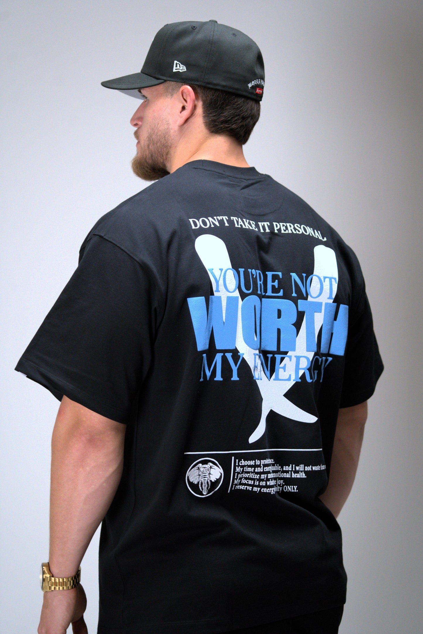 Person wearing a black t-shirt with a graphic and text on the back, standing against a plain background.