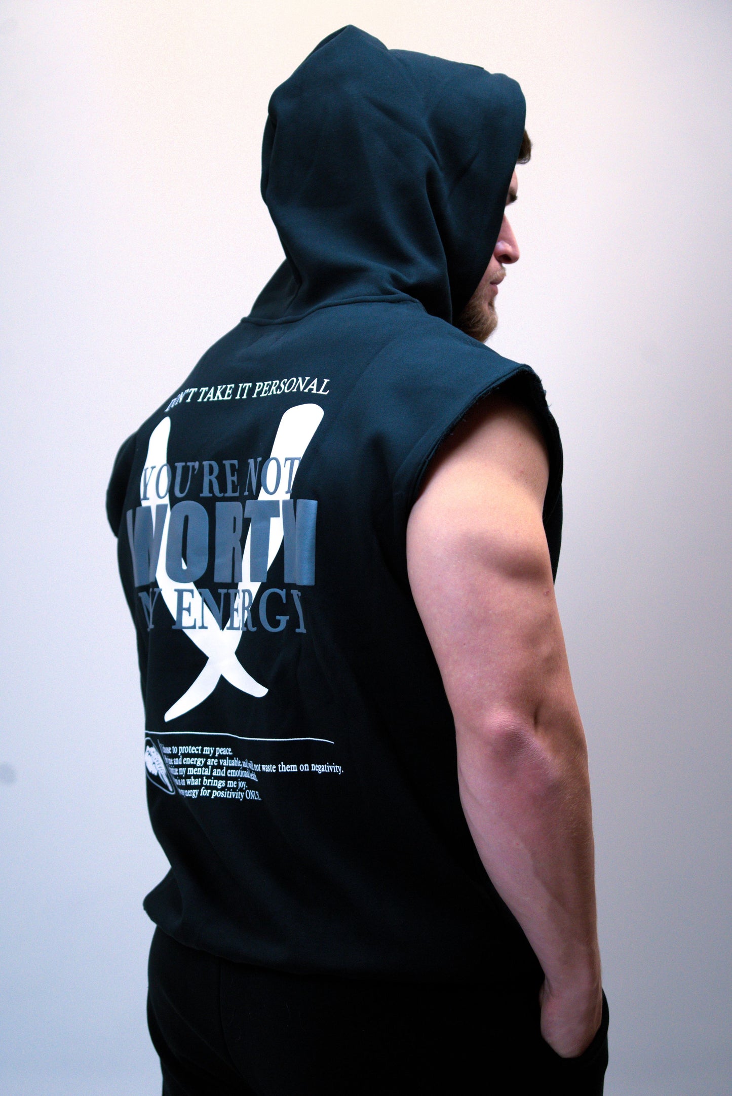 Person wearing a sleeveless hoodie with text on the back against a plain background